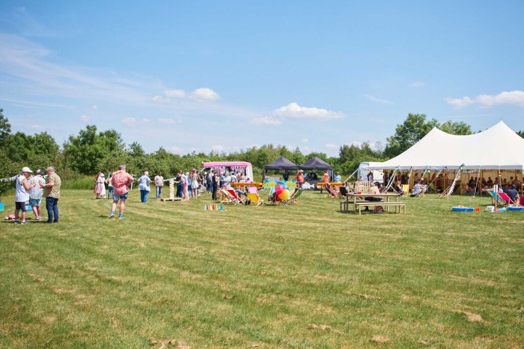 A summer party taking place in a field, complete with a marquee, two gazebos and an ice cream van.