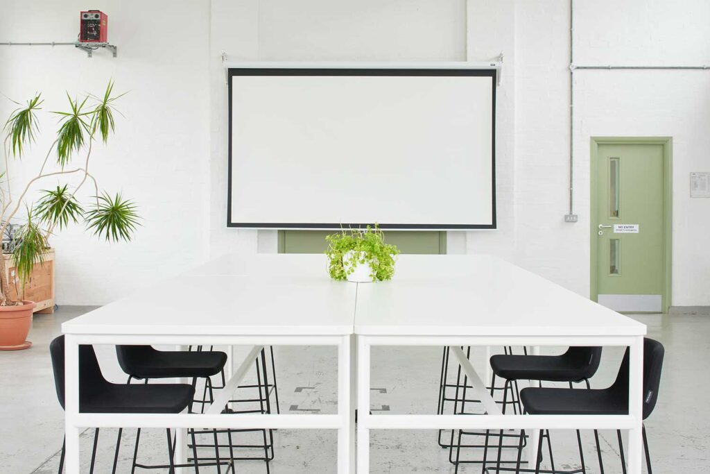 A meeting table with chairs around it and a large projector screen at one end.