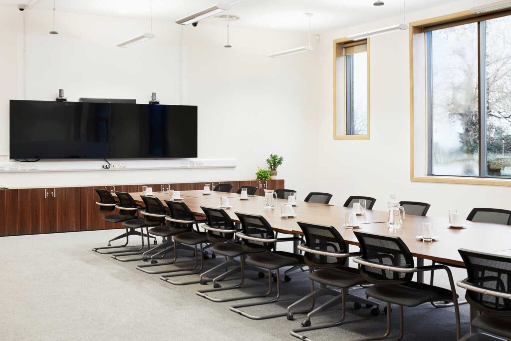 A large meeting room with a long table and lots of chairs, and a large screen at one end of the room.