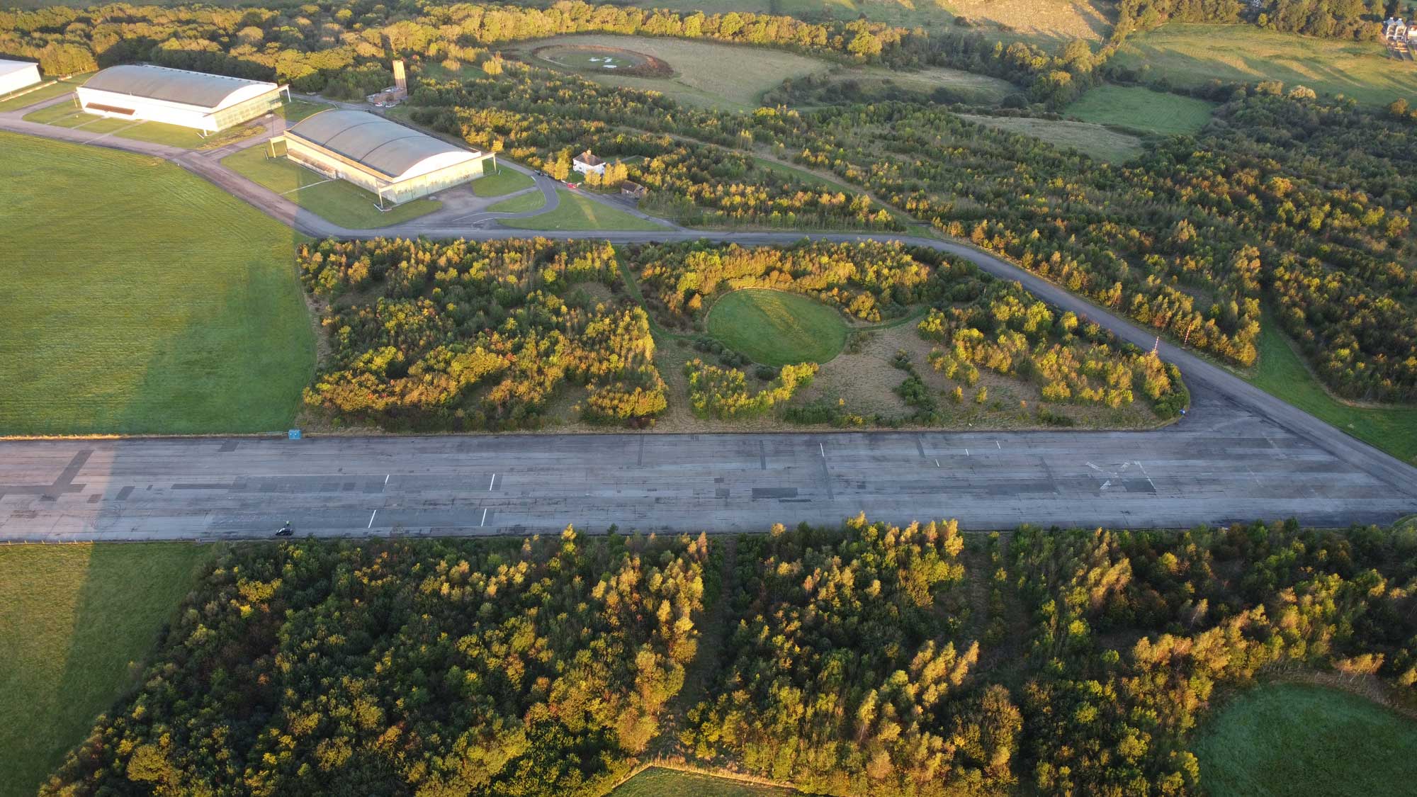 An aerial view of an old runway and two aircraft hangars in the English countryside.